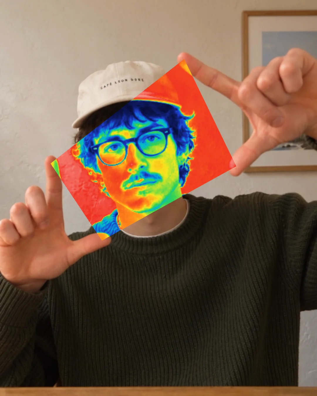 A man frames his face between his fingertips, and the portal between them shows it in the Thermal filter’s heat colours